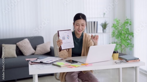 Young Asian professional presenting business analytics report during video conference from bright home office workspace