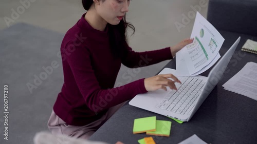 Young Asian Gen Z professional analyzing financial report while working remotely on laptop at modern home office desk