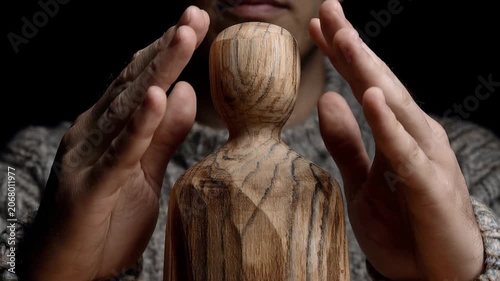 Human hands shielding a wooden figure, A wooden statue of a man with his hands raised