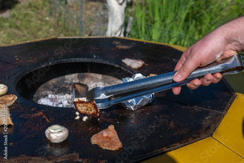 Obraz na płótnie Close-up of tongs turning seared meat on a hot flat-top grill at a summer barbecue