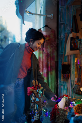 Foto Happy young hispanic woman choosing christmas gifts in urban boutique, holiday shopping, winter vacation, local store window display, authentic representation, real people, lifestyle mood
