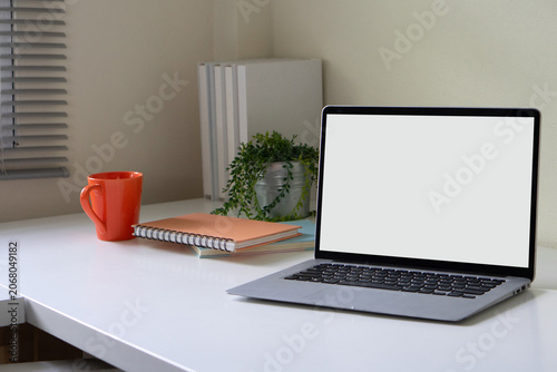 A minimalist workspace setup features an open laptop with a blank white screen next to an orange mug.