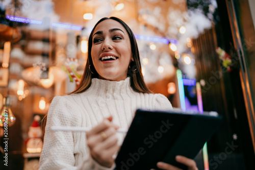 Fotografie Pensive young female professional looking up while working on tablet, ambitious woman dreaming about career growth and financial freedom, digital nomad lifestyle in urban setting, success