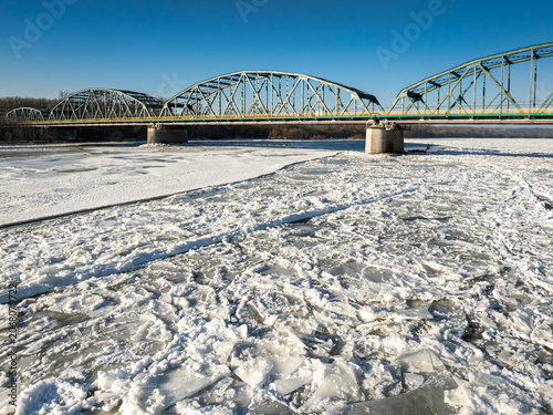 Old metal bridge with traffic over river with ice floes.