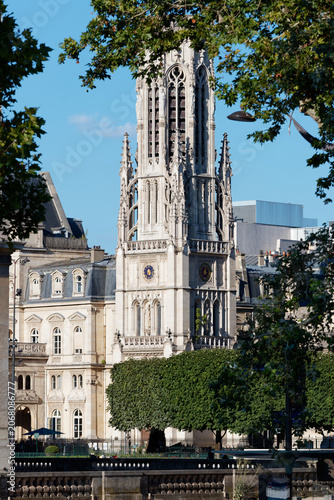 Majestic Flamboyant Gothic bell tower of the Saint-Germain-l'Auxerrois church rises above the rooftops near the Louvre in Paris, framed by lush summer trees