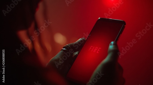 Close up of smartphone held in hand displaying the word fire on a red screen with dark background and soft lighting creating an atmospheric effect