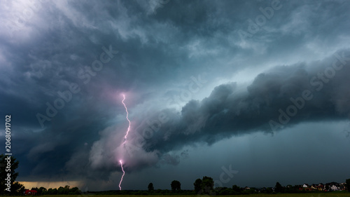 Dramatic lightning bolt striking from a powerful shelf cloud during severe summer thunderstorm. Extreme weather landscape