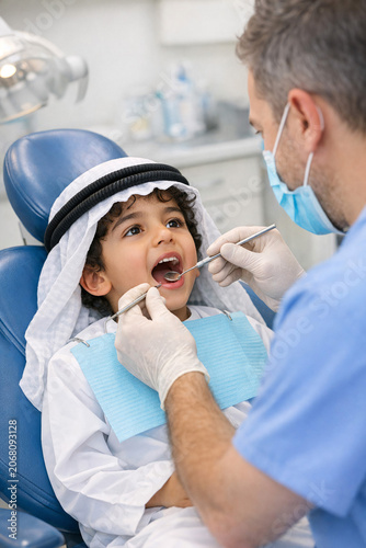 A young child wearing a mask and having his teeth examined by a dentist with medical equipment in the background.