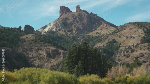 Wide shot of the prominent Cerro Montura Chilena mountain peak towering over a forested hillside in Valle Encantado, Patagonia, Argentina.