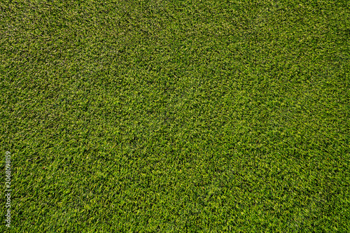 Artificial green soccer turf texture in warm evening sunlight. Synthetic grass field pattern during golden hour. Sunset light on football pitch lawn
