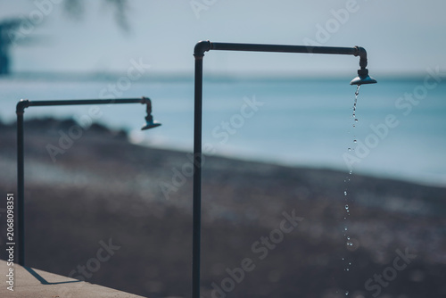 Valokuva Water trickles gently from two metal taps near a calm beach, creating a serene m