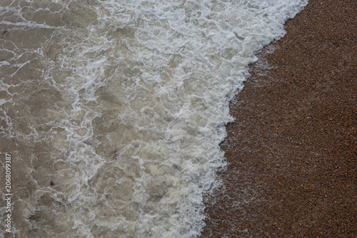Waves crash on sand at the beach during a cloudy day in the early afternoon with a calm scene of nature