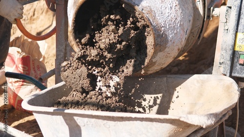 фотографія Concrete Pouring From Mixer Into Wheelbarrow Via Chute, Wet Flow And Granular Te