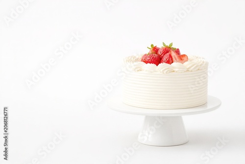 White cake sits on pedestal, decorated with strawberries. Creamy frosting swirls around the base, elegant and sweet. Fresh strawberries add vibrant red contrast against soft white
