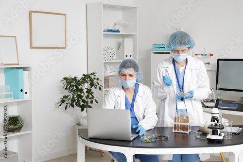 Female scientist working with laptop and Petri dish at table in laboratory