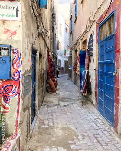 Narrow Alley with Colorful Doors and Hanging Rugs in Essaouira Medina, Morocco