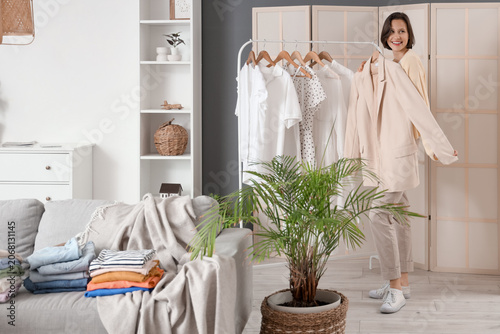 Young woman with jacket near rack of clothes at home