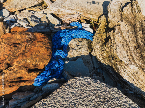 Photography Drone inspection view of rocky coastline with thick blue marine rope washed asho
