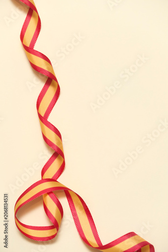 Spanish flag colored ribbon on beige background in a design with copy space. Concept: celebration of national holidays or national victories.