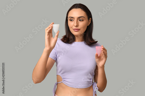 Beautiful young woman with menstrual cups on grey background