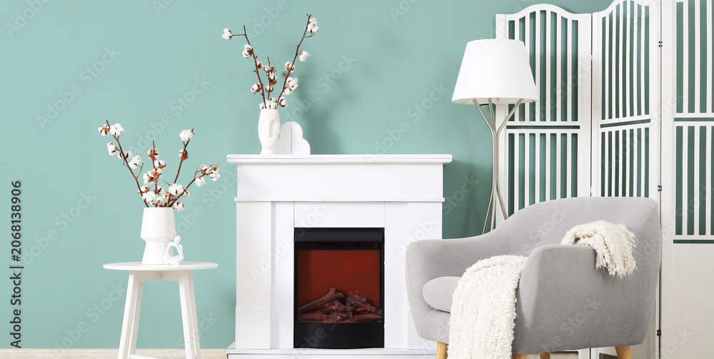 Obraz premium Interior of stylish living room with grey armchair, fireplace and cotton flowers