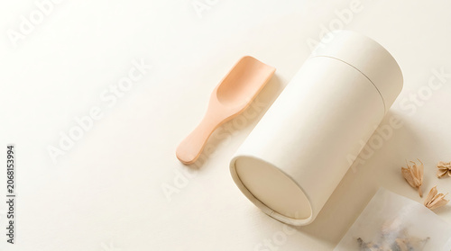 Blank cylindrical paper tea tin mockup with a small wooden scoop on a beige background