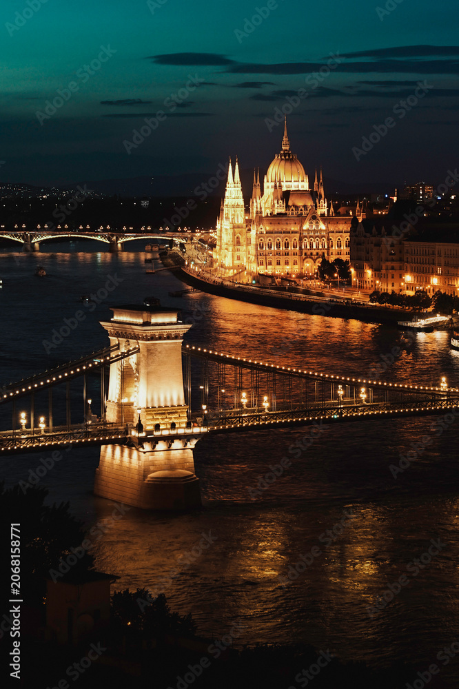 Obraz premium The illuminated Hungarian Parliament Building and Chain Bridge reflected on the Danube River after sunset.