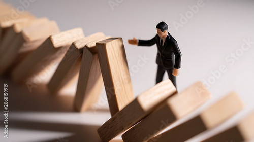 Tiny Business Executive Miniature Doll Stop Falling Domino Blocks from Chain Reaction, Crisis Management and Risk Aversion Concept