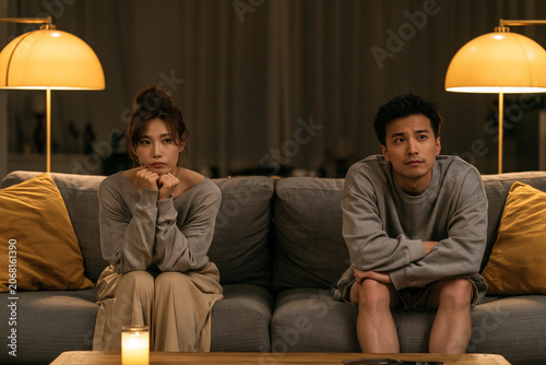 Couple sits on couch in living room and watches television during evening time
