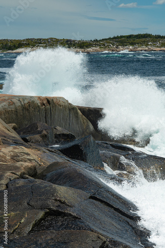 A dramatic scene at Peggy’s Cove, Nova Scotia, featuring powerful Atlantic Ocean waves crashing against rugged, glaciated granite rocks.