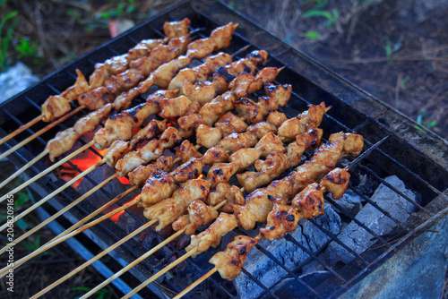 Tableau sur toile Multiple chicken satay skewers grill over glowing, hot charcoal embers on a trad