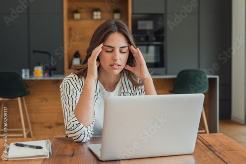 Foto Woman struggling with a stress-related headache at a laptop in her home office,
