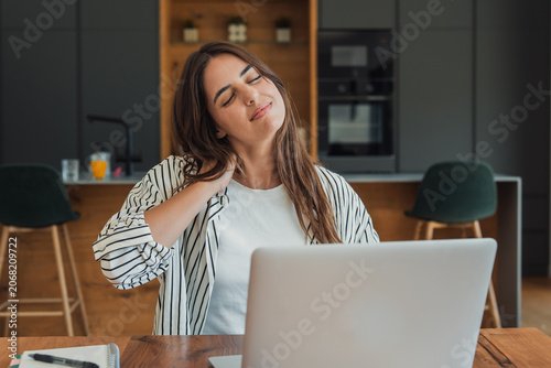 Tableau sur toile Young woman working on laptop massaging her stiff neck and shoulders, experienci