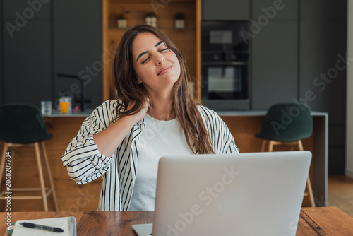 Foto Young woman experiencing neck pain and stiffness while working from home, massag