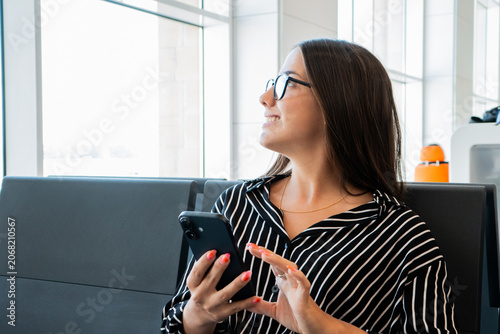 Foto Young woman wearing glasses and a striped shirt, holding a mobile phone and look