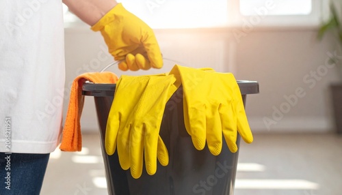 Gloved hand holding a bucket brimming with cleaning essentials, symbolizing preparation for meticulous hygiene, sanitation, and household maintenance tasks