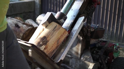 Side view of a man operating a hydraulic log splitter, carefully adjusting a thick piece of wood to cut it into smaller, manageable firewood logs