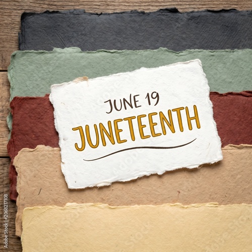 A torn paper sign reading June 19 Juneteenth on a wooden background with colorful paper strips