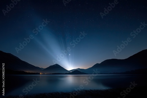 Majestic mountains frame a serene lake under a starry night sky, illuminated by a bright light