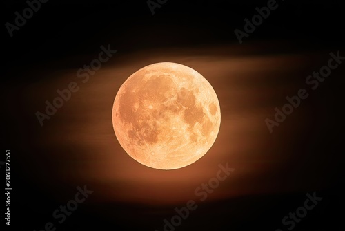 Large, glowing orange orb in the night sky, partially obscured by faint clouds