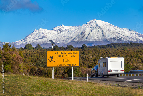 Mt Ruapehu, New Zealand, winter snow. Warning sign for traffic. NZ's largest active volcano. Tongariro National Park. Car with caravan on Desert Road.
