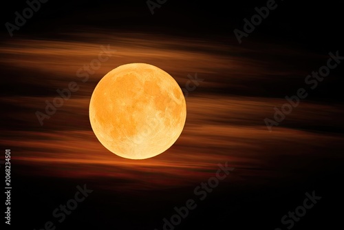 A bright orange full moon emerges through wispy, dark, fiery clouds