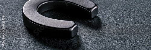 Close-up of a dark, metallic horseshoe on a textured dark gray surface