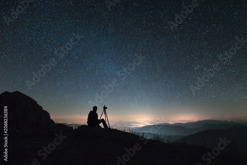Silhouette of a person with a camera on a tripod gazes at a starry night sky