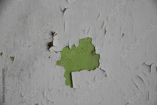 Close-up texture of peeling white paint revealing a bright green layer on a wall