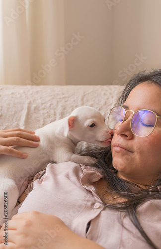 Woman with glasses working from home on laptop with white pinscher puppy