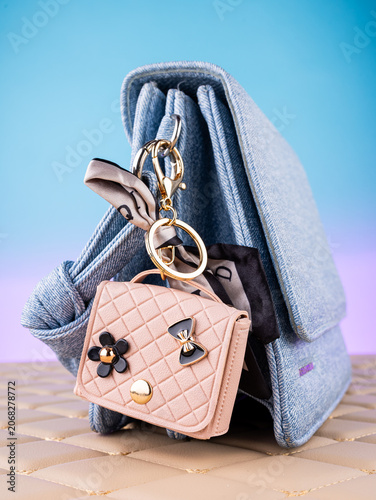 Close-up of a leather mini bag-shaped keychain with bow and charms on a  blue bag. Elegant and charming accessory.