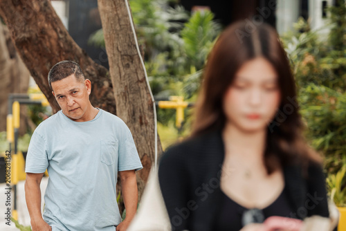 Photos A young Southeast Asian woman checks her phone, unaware that an unfamiliar man watches and trails her from behind