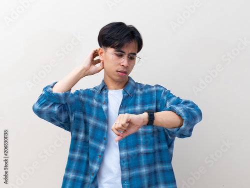 Принти на полотні Confused young Asian man with glasses looking at his wristwatch while scratching