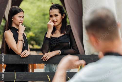 Tableau sur toile Two young Southeast Asian women react with awkward and uncomfortable expressions while an older man waves at them outdoors